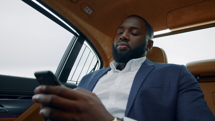 Closeup guy typing mobile phone in car. Afro businessman chatting smartphone
