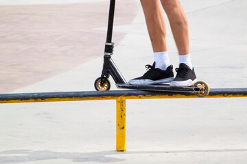 Fototapeta na wymiar rider on stunt kick scooter slides along edge of metal ramp in skate park