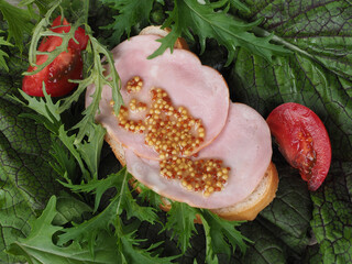 Sandwich with white bread, ham and French grain mustard, tomatoes on the background of fresh green...