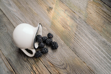selective focuse berries spilled out of a jug, blackberry on a wooden background. natural...