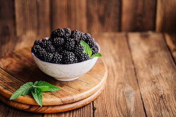 Fototapeta na wymiar berries on a wooden background. blackberries in a plate, decorated with mint. fresh summer vitamins. vegan, raw food