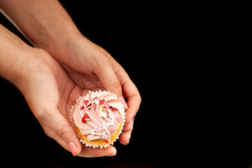 Female hands hold an appetizing, beautiful cupcake on a black background. Unhealthy, sweet food concept