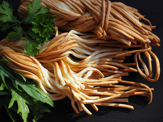 Smoked braided cheese pigtail, spicy herbs arugula and parsley on a dark background, closeup....