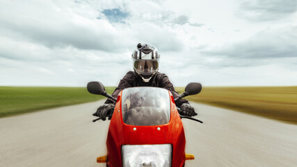 Motorcyclist rides a sports motorcycle at high speed forward, along the highway, looks at the camera