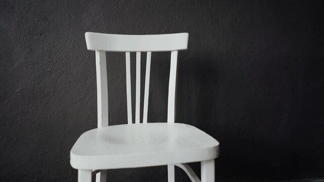 Against the grey wall stands an old white chair. Close-up