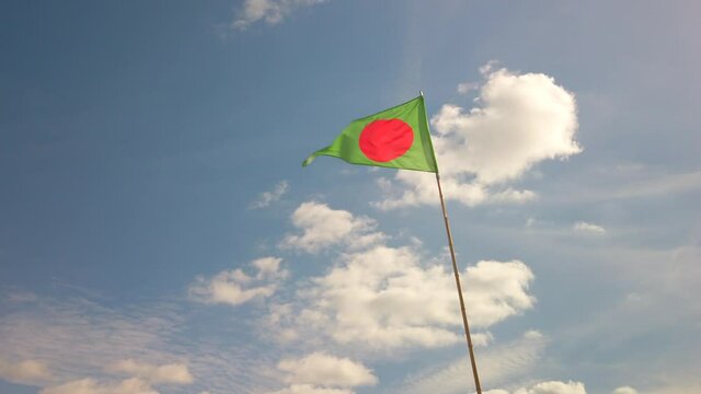 Green triangle flag with red dot fluttering in the wind against blue sky at a beach in Anglet, France. It indicates a surfing area.