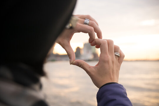 Close-up Of Woman Hands Making Heart Shape Against Sea During Sunset