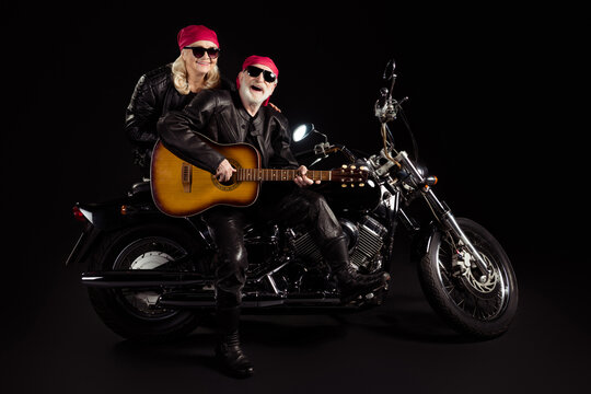 Photo of aged bikers man lady couple sit chopper moto feel young rock bike festival meeting play sing guitar band wear trendy rocker leather jacket pants isolated black color background