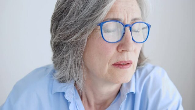 Mature lady in glasses looking out window and thinking, tired of working