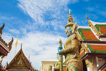 Fototapeta premium A demon guardian statue with a Great golden stupa in Wat Phra Kaew against the sky, Temple of the Emerald Buddha Wat Phra Kaew is one of the most famous places in Bangkok, Thailand