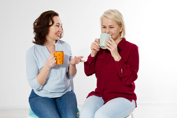 Two healthy and beautiful middle aged women drinking tea and talking isolated on white background. Woman support woman. Happy menopause concept.