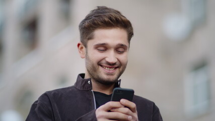 Smiling guy using phone on street. Happy man looking phone screen outside.