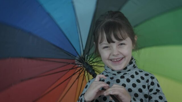 Colorful umbrella in the house. Cheerful little girl with a multi-colored umbrella.
