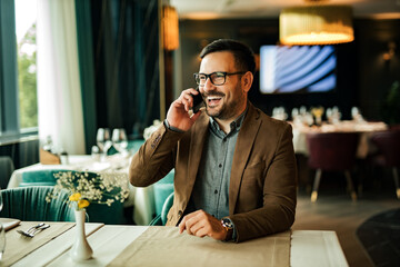 Portrait of a handsome man sitting in the restaurant and laughing while talking on smart phone.