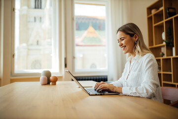 Cheerful young woman working on laptop at home office, portrait.