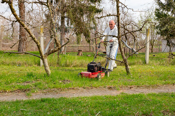 Farmer in protective clothing is mowing a lawn in a garden with a petrol lawn mower