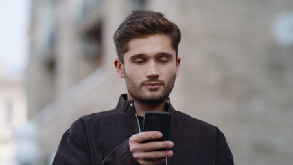 Surprised man using phone outside. Smiling guy reading message on phone outdoors