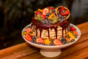 Delicious handmade layered cake decorated with chocolate glaze, strawberries, blueberries, carambola star fruit and ice cream cone on nature tropical background