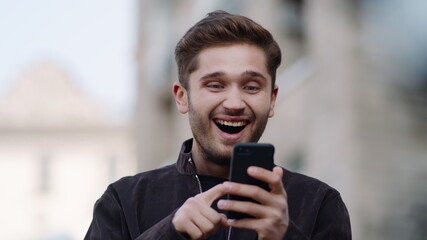 Happy man using phone outside. Surprised guy using cell phone outdoors.