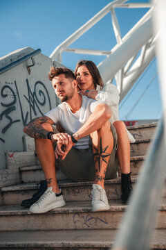 Shooting fotografico di due giovani fidanzati e modelli in posa seducente mentre sono seduti assieme sulle scalinate di un'area urbana d'estate