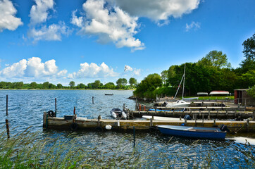 Obraz premium A beautiful coastline at a lake in Germany, Schlei, with a tiny boat at a pier in front of beautiful blue sky and white clouds