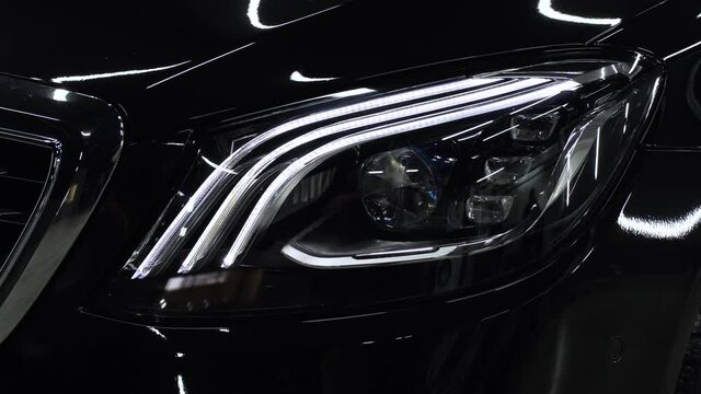 The oversized headlights of a premium black car. Close-up of the front headlights
