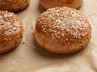 baked sesame buns on brown parchment paper, ingredient for a hamburger