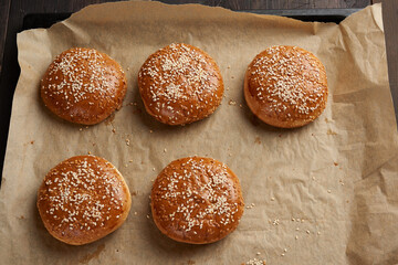 baked sesame buns on brown parchment paper, ingredient for a hamburger