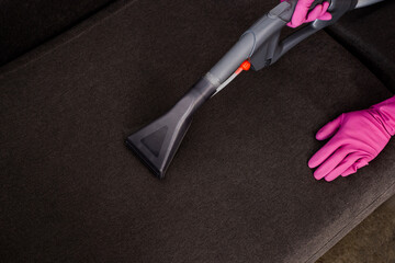 Cropped view of cleaner in rubber gloves cleaning couch with vacuum cleaner