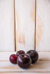 Some dark ripe plums on a white wooden wall and table, with copy space