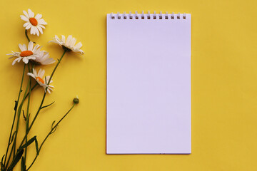 bouquet of flowers and a blank notebook on a yellow background. Top view, flat lay