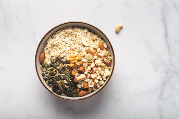 Ingredients for healthy homemade granola with Gluten Free Rolled oats or porridge oats, variety of chopped nuts and seeds, and maple syrup. Preparation for cooking at home, all mixed in bowl.