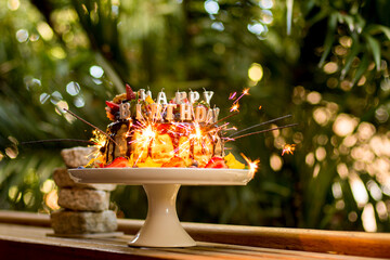 Delicious handmade layered cake decorated with sparkles, happy birthday candles, chocolate glaze,...