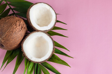 Ripe half cut coconut with cream and green leaves on a pink background.