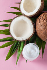 Ripe half cut coconut with cream and green leaves on a pink background.