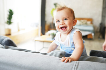 Portrait of a persistent funny little baby boy sitting on gray sofa and smiling or laughing