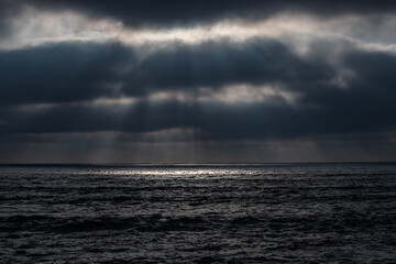 Fototapeta na wymiar trouées de soleil à travers les nuages noirs qui font des taches sur la mer