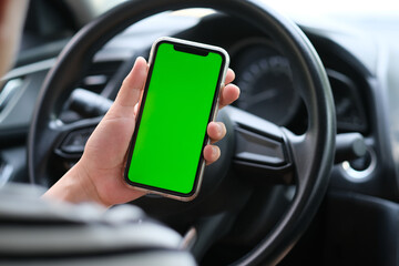 over shoulder of man holding green screen smart phone inside car. blur background