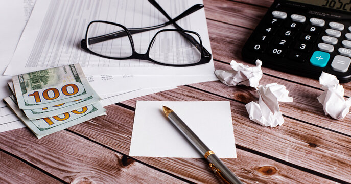 On a wooden table are glasses, money, a calculator and a pen. Close-up of the working area. Business concept
