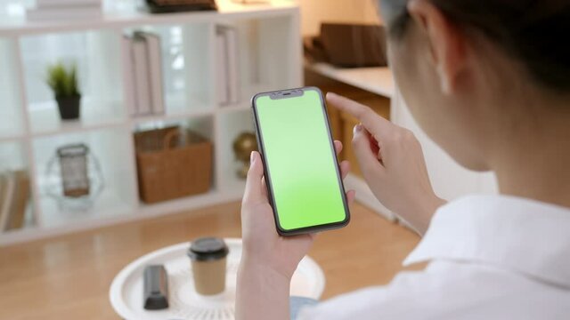 Woman holding mockup smartphone green screen with type message on the sofa at home.