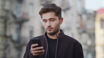 Hipster guy receiving message on phone outside. Smiling man looking phone screen
