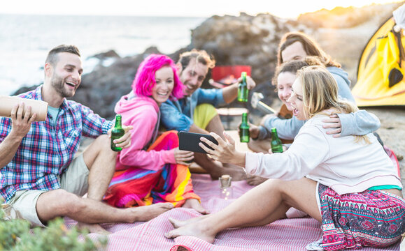 Adult friends taking selfie with smartphone at camping beach party outdoor - Happy people having fun doing barbecue and drinking beer - Focus on right girl hand - Alternative fest concept