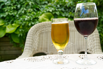 A pint of beer and a glass of red wine set against a green plant, on white table.