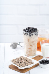 Bubble milk tea with tapioca pearl topping ingredient, famous Taiwanese drink on white wooden table background in drinking glass, close up, copy space