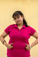 Indian female model looking down unhappy with her fat belly in yellow background with copy space for text