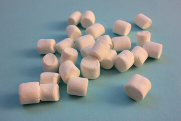 Little white marshmallows on blue background with copy space. Selective focus