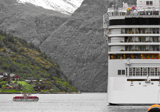 Rear view of stern of modern cruiseship or cruise ship liner and tender in Geirangerfjord Norway with breathtaking and beautiful nature and mountain landscape scenery in background in Europe&acute;s Alaska
