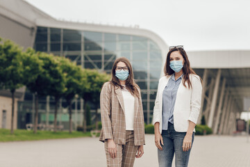 Two young women on the background of a building outdoors, with medical masks on their faces.
