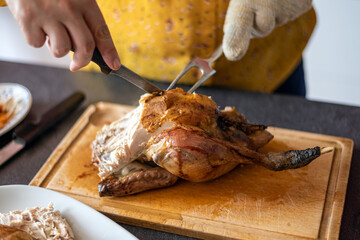 Caucasian woman carving a roasted chicken on a wooden platter, using a knife and a fork.