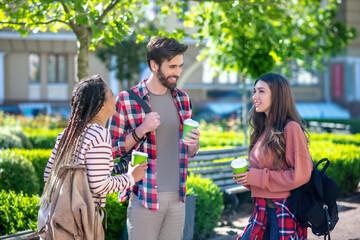 Guy with camera and two girls with backpacks drinking coffee